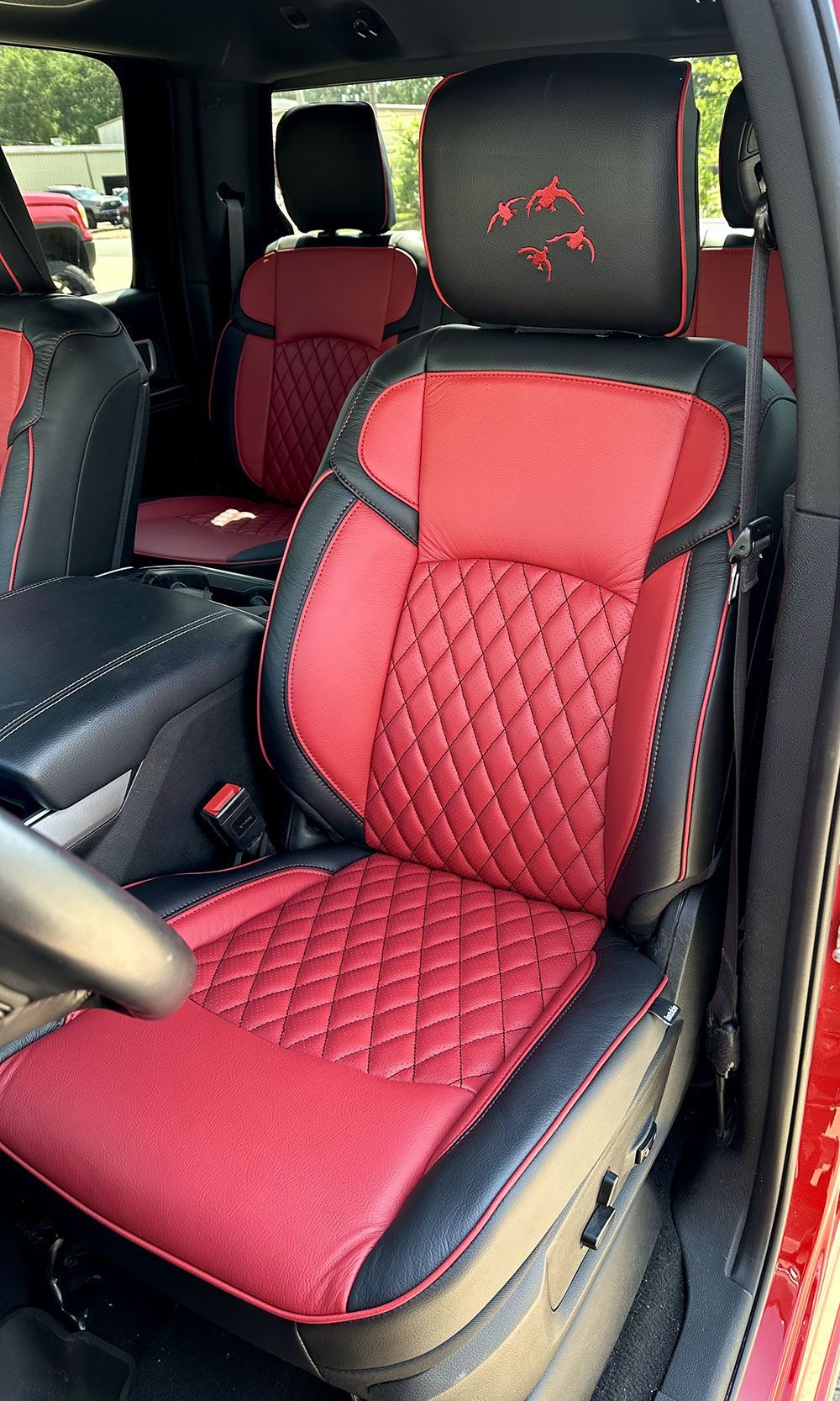 Red and black leather car seat with diamond stitching, logo on headrest.