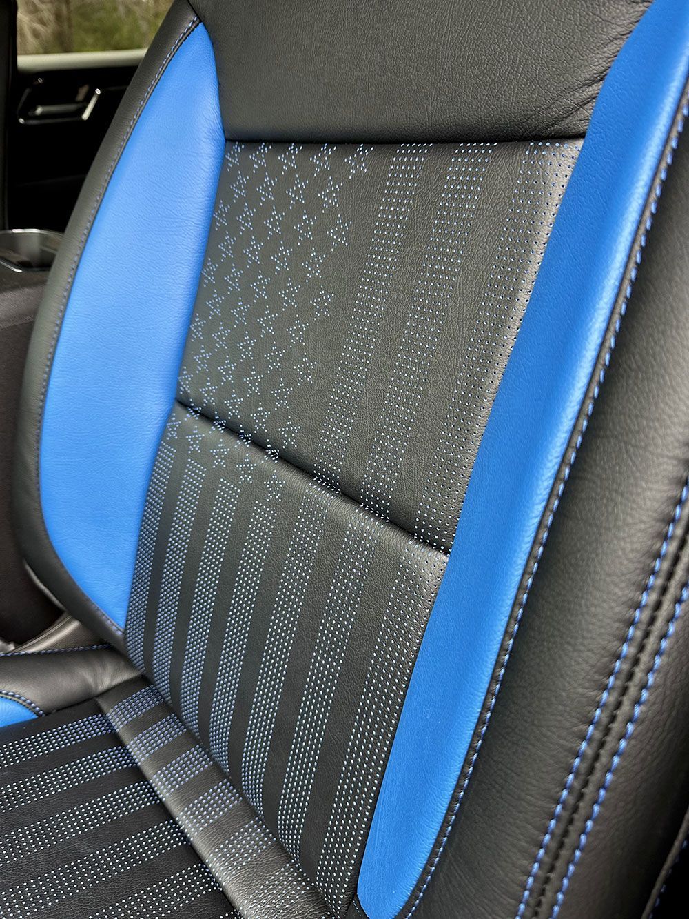 Black and blue car seat with textured center panel and blue side panels. Blue stitching visible.