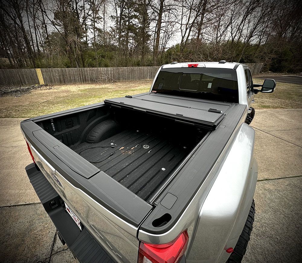 Silver pickup truck bed with closed black tonneau cover, parked outdoors.