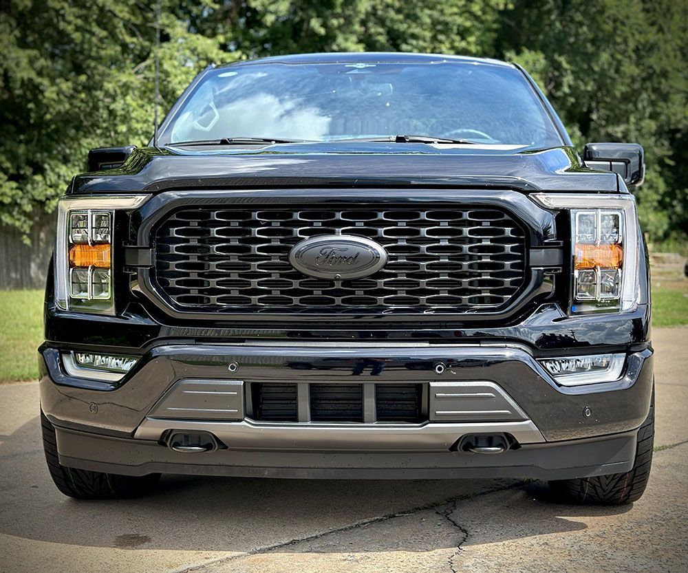 Black Ford F-150 pickup truck with black grill and headlights, parked on asphalt.