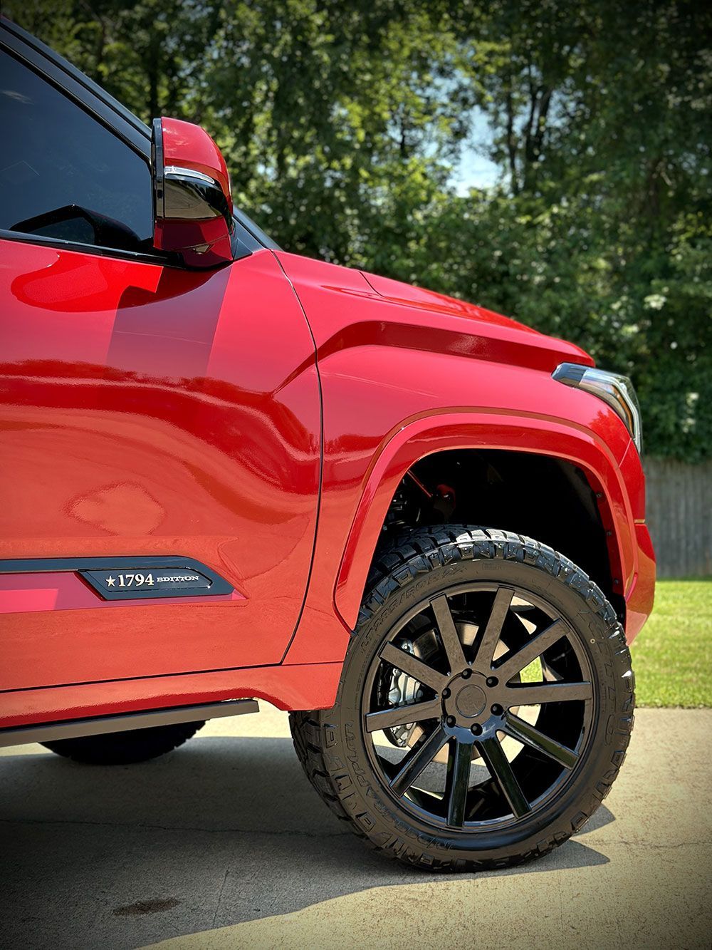 Red truck with black wheels parked on a driveway.