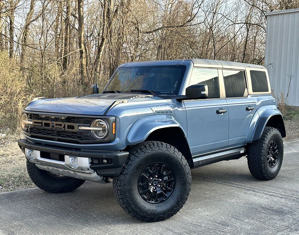 Blue Ford Bronco SUV, black wheels and tires, parked outdoors.