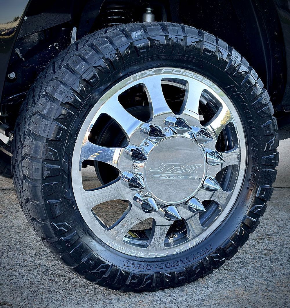 Close-up of a chrome truck wheel with a black, textured tire. The wheel has a custom center cap.