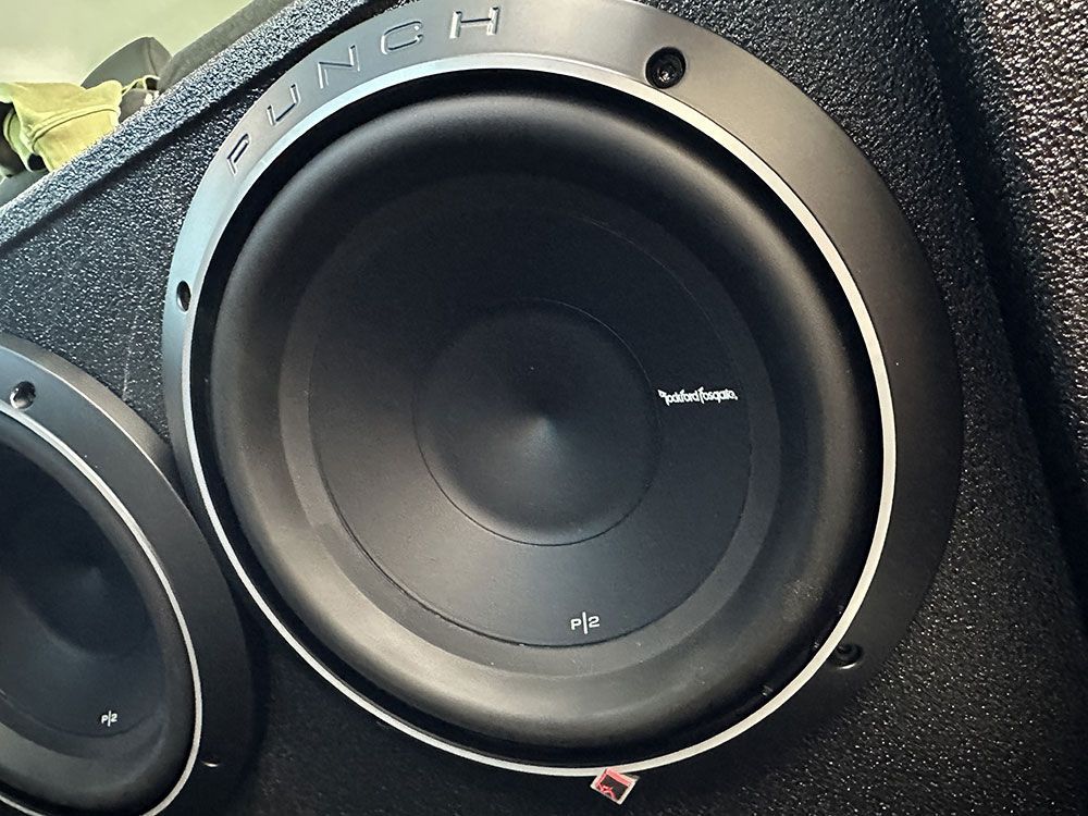 Close-up of a black car subwoofer with a silver trim, mounted in a black enclosure.