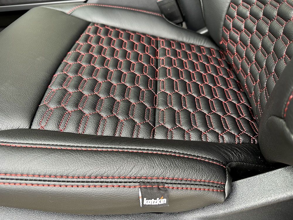 Black car seat with red stitching in a honeycomb pattern.