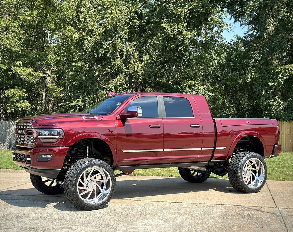 Burgundy lifted pickup truck with chrome wheels parked outdoors.