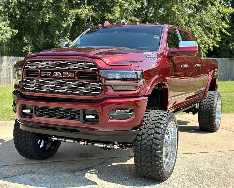 Red, lifted RAM truck parked outside with large chrome wheels and tires.