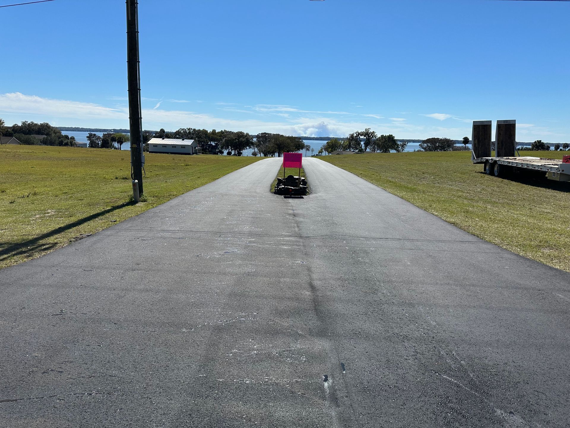 Asphalt road with a red and black vehicle driving towards a distant body of water.
