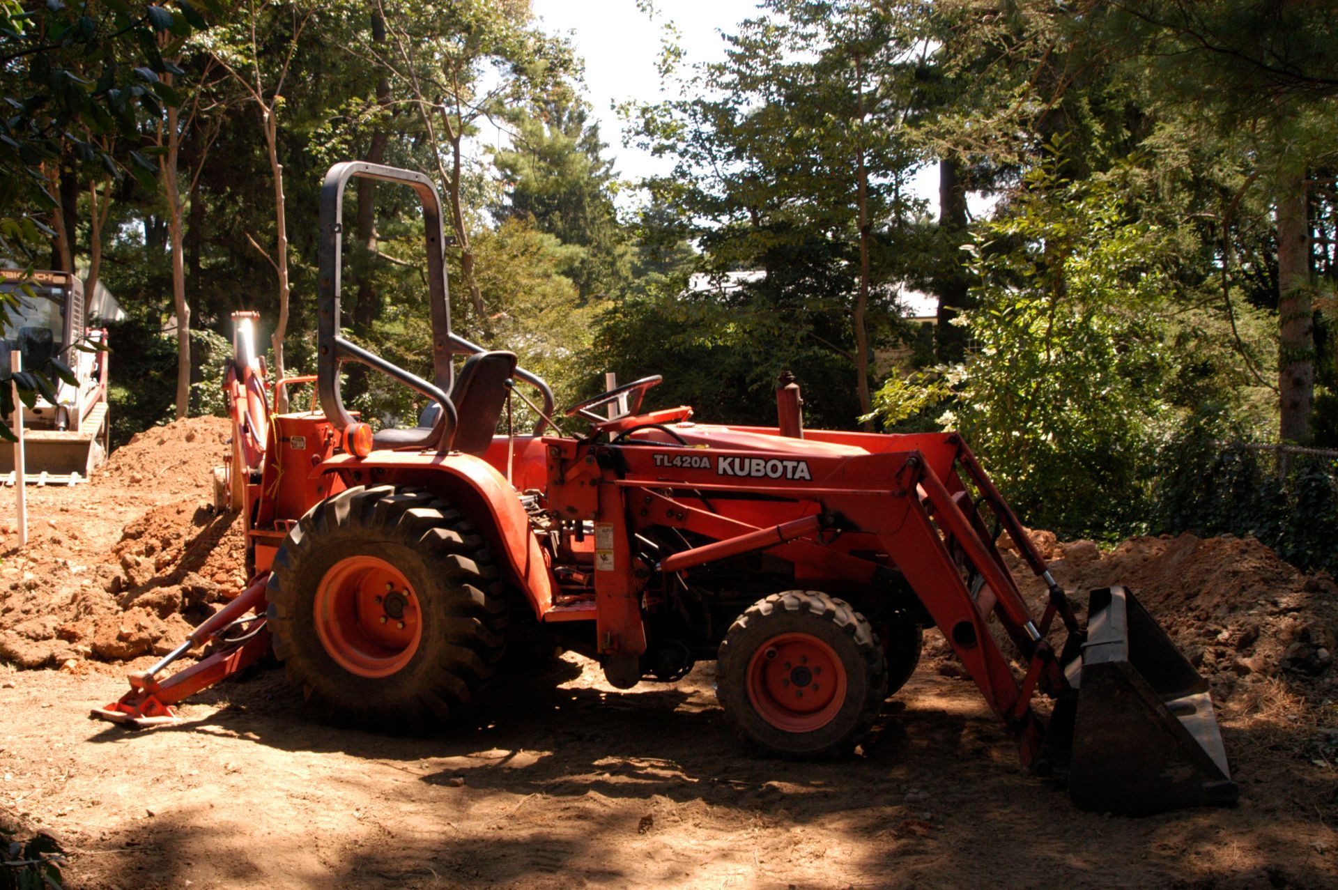 Orange Kubota tractor with a bucket in a wooded area.