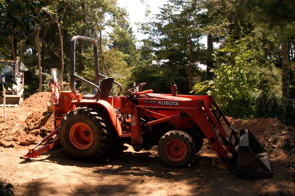 Orange Kubota tractor with a bucket in a wooded area.