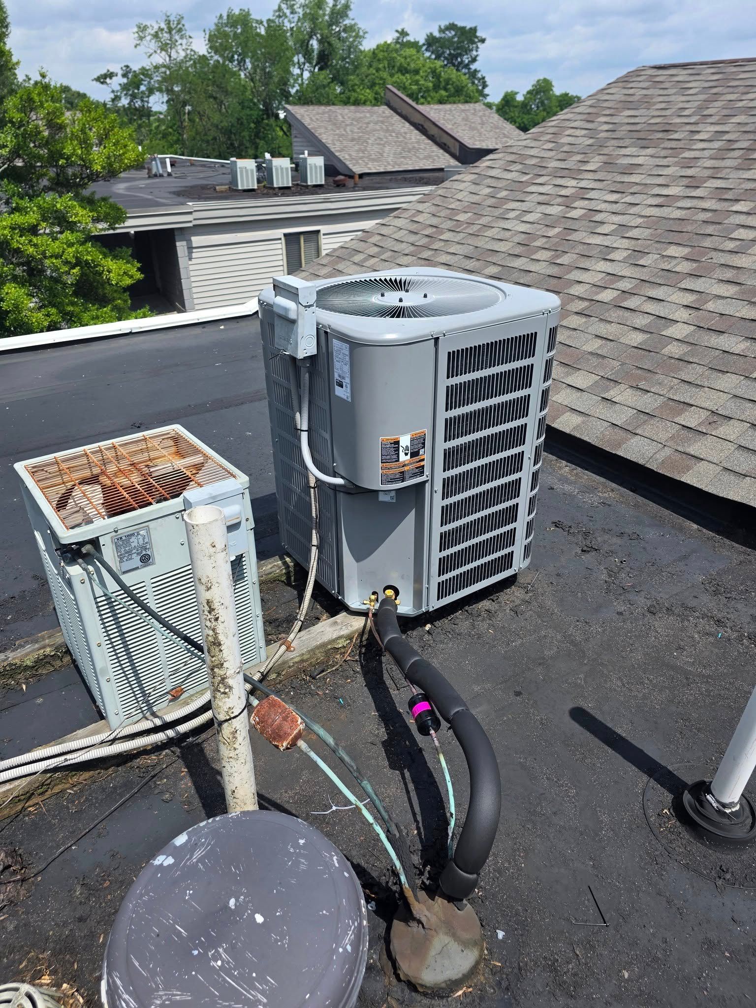 Two rooftop air conditioning units on a black flat roof. A newer gray unit and an older corroded unit.