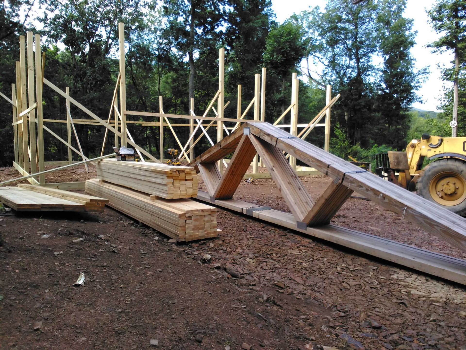 A large piece of wood is laying on the ground next to a yellow tractor.