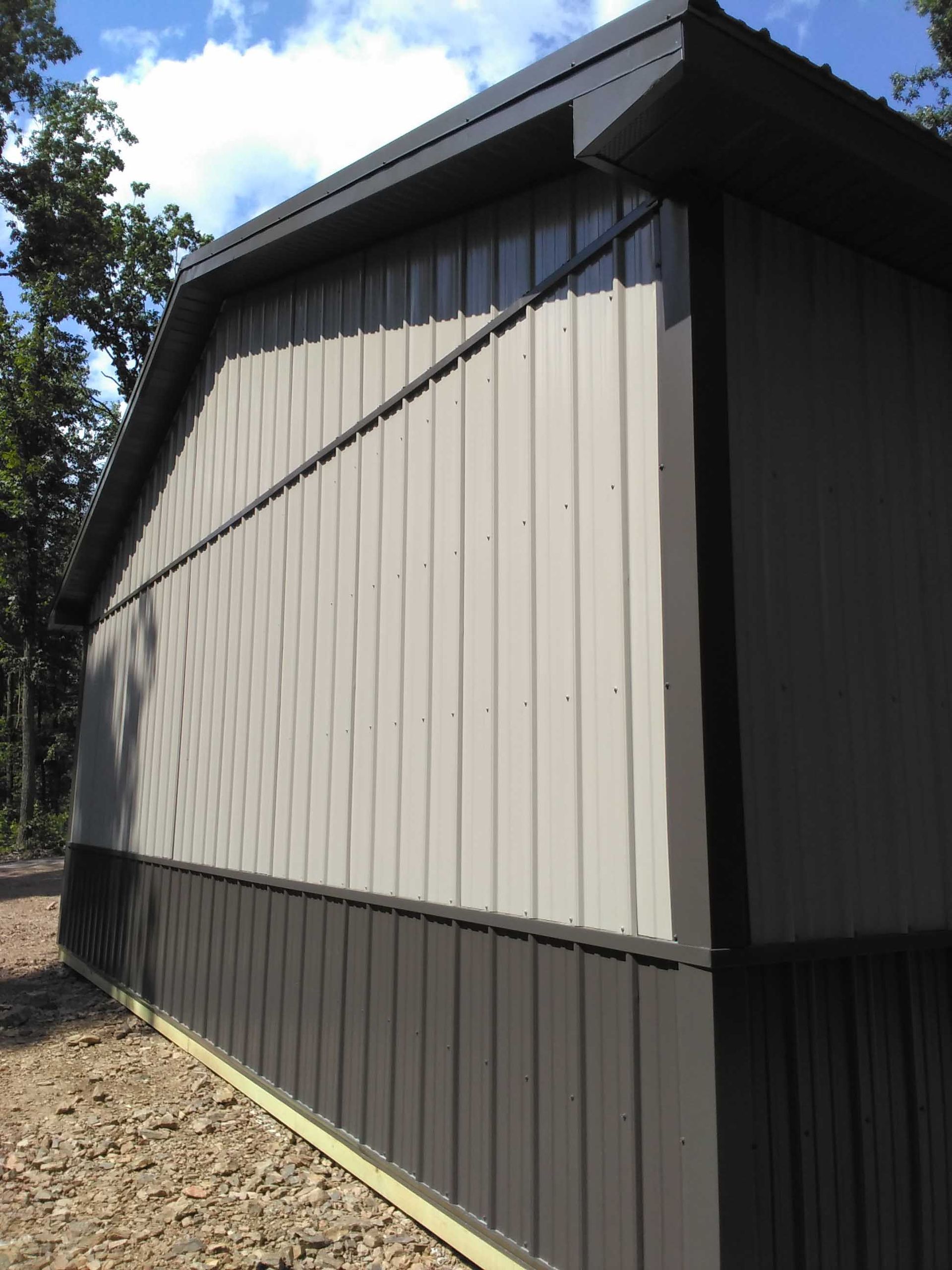 A gray and black building with a roof is sitting on a dirt road.