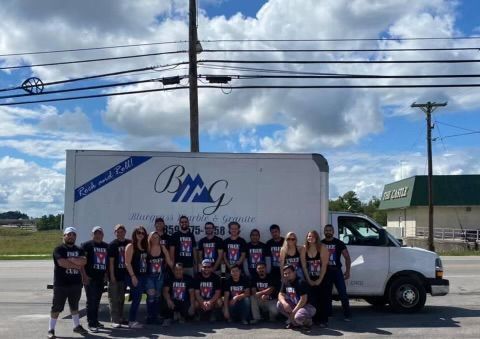 A group of people are posing for a picture in front of a moving truck