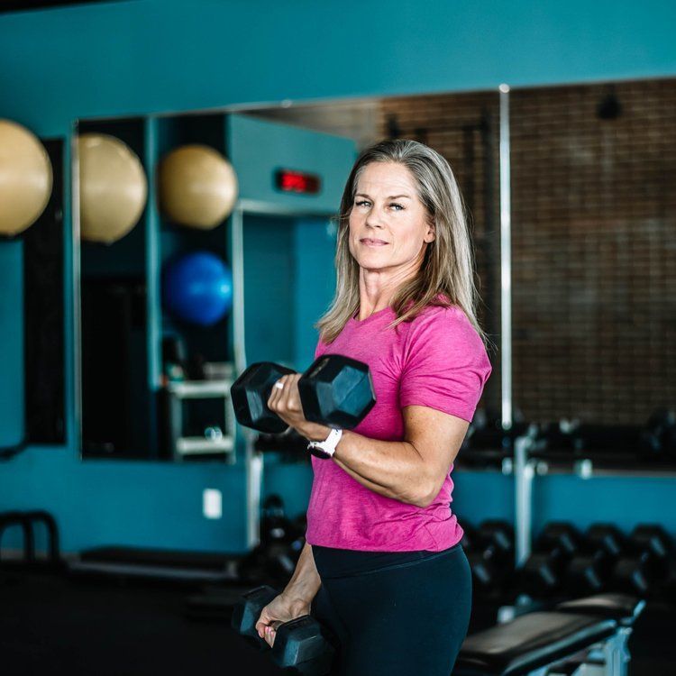 A woman in a pink shirt is holding a dumbbell in a gym.