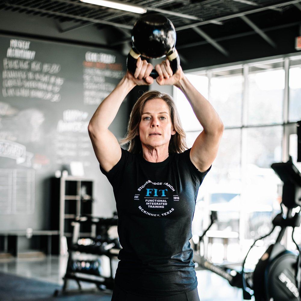 A woman is lifting a kettlebell over her head in a gym.