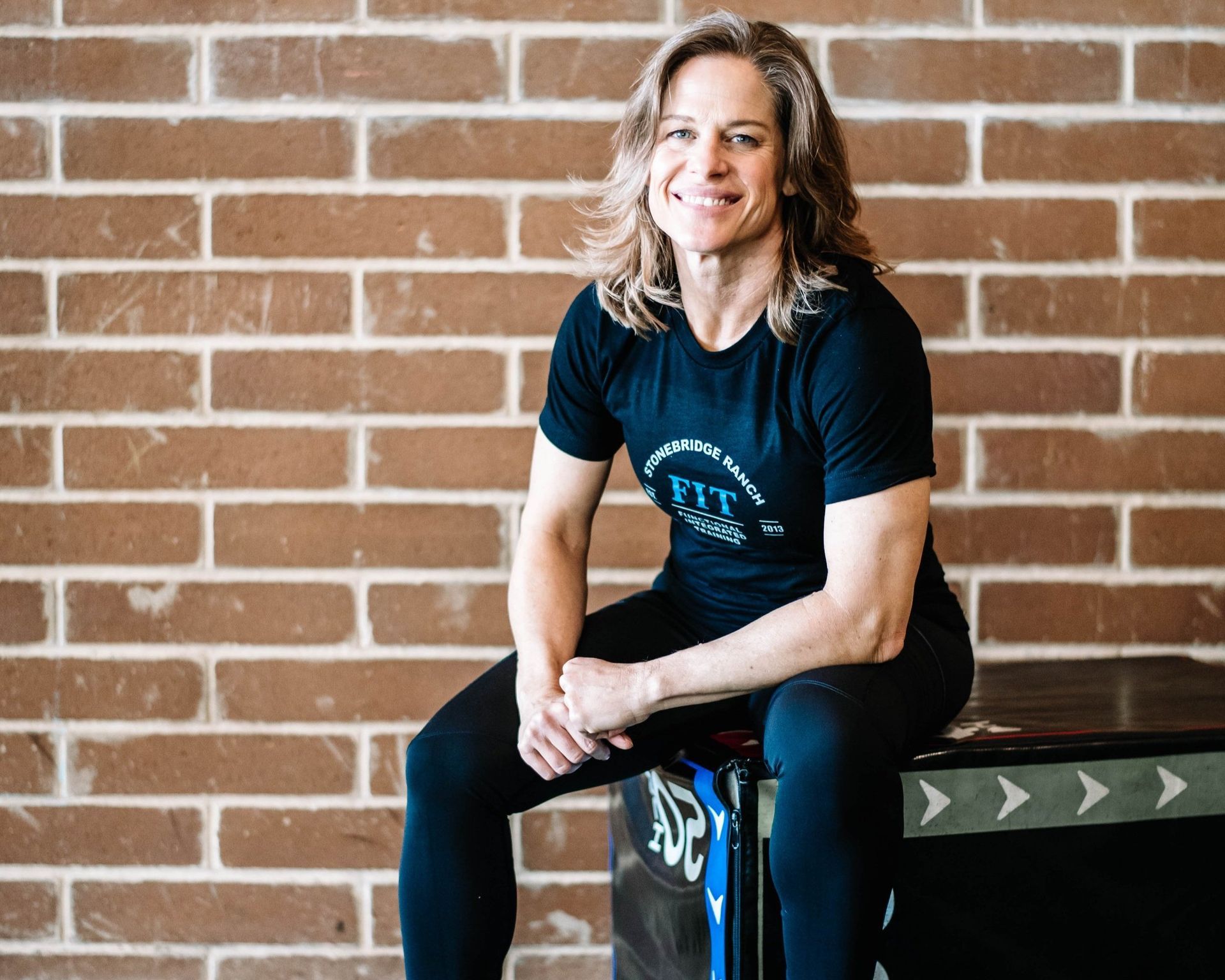A woman is sitting on a box in front of a brick wall.