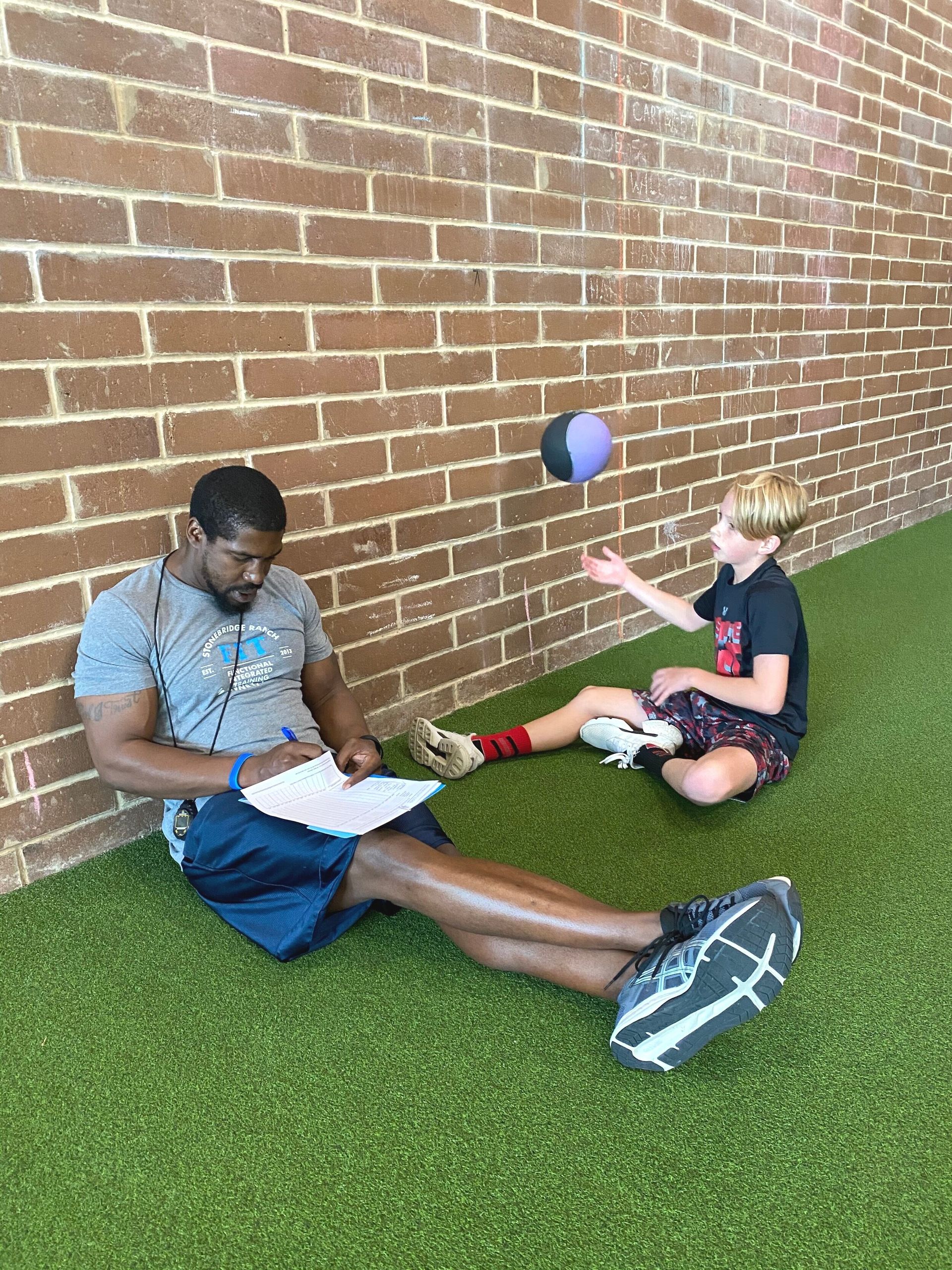 A man is sitting on the ground talking to a young boy.