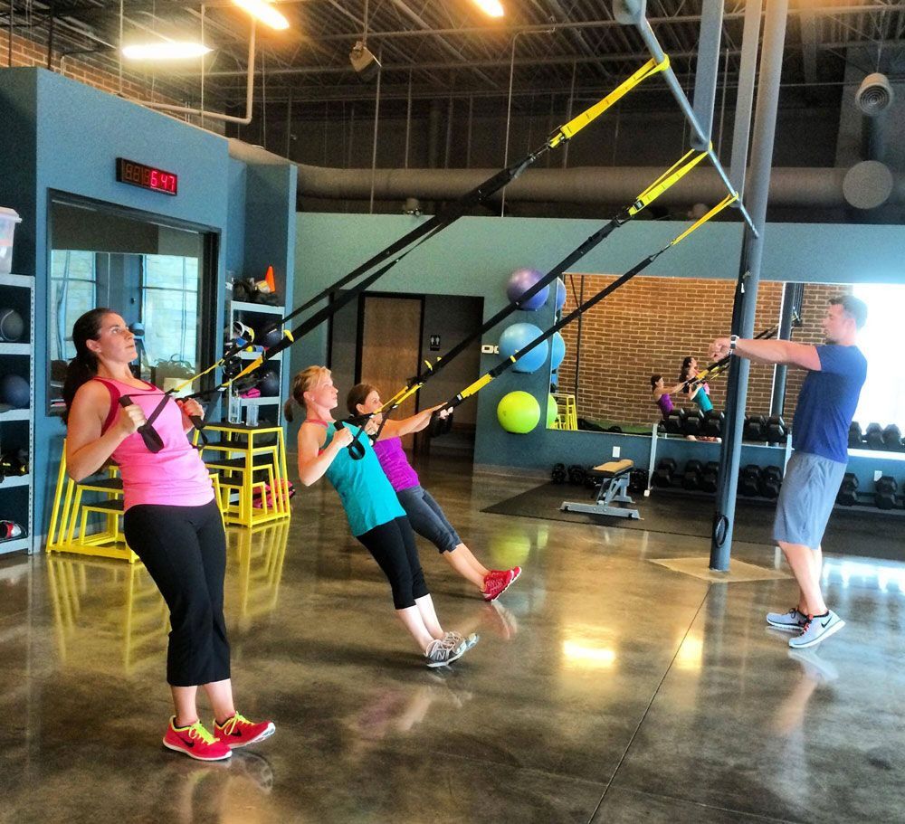 A group of people are doing trx exercises in a gym