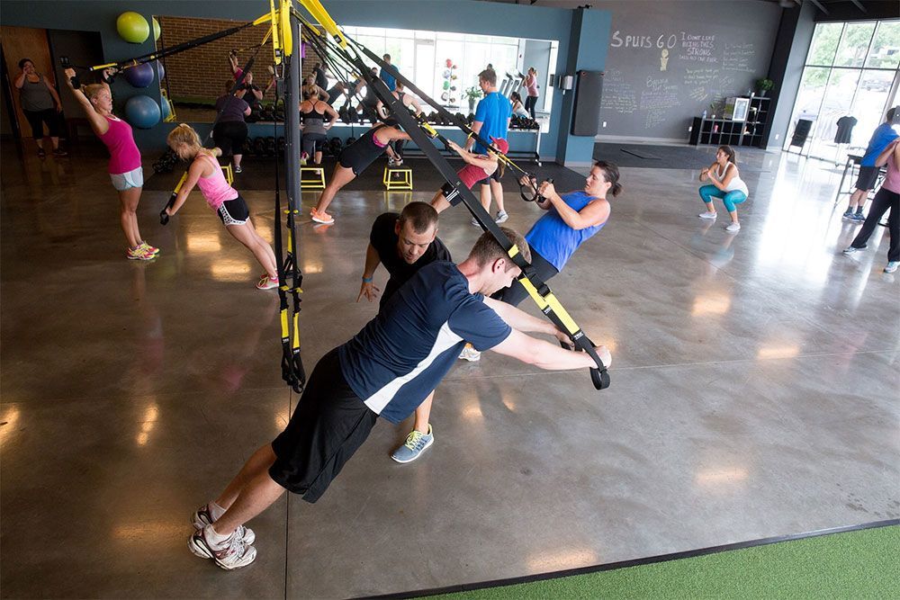 A group of people are doing trx exercises in a gym.