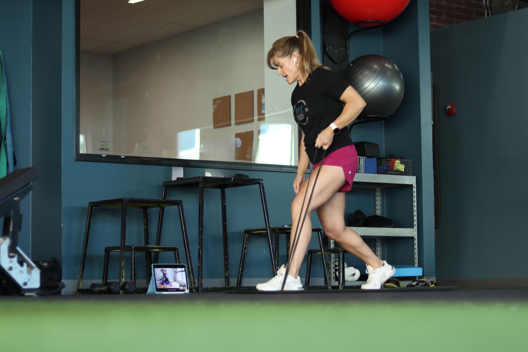 Woman exercising with resistance band in gym. She’s lunging, holding the band with both hands, and watching a screen.
