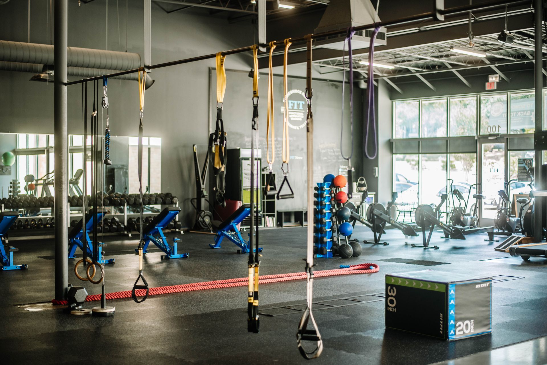 Gym interior with training equipment, including TRX straps, weights, and cardio machines.