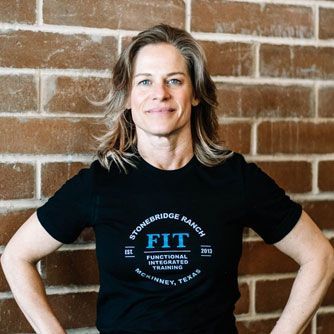 A woman wearing a black t-shirt with the word fit on it is standing in front of a brick wall.