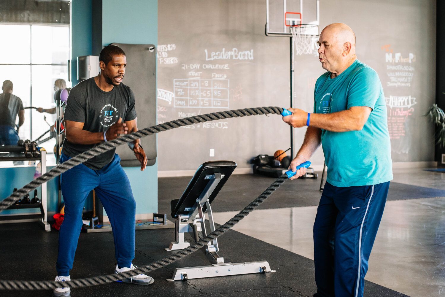 Two men are working out with ropes in a gym.