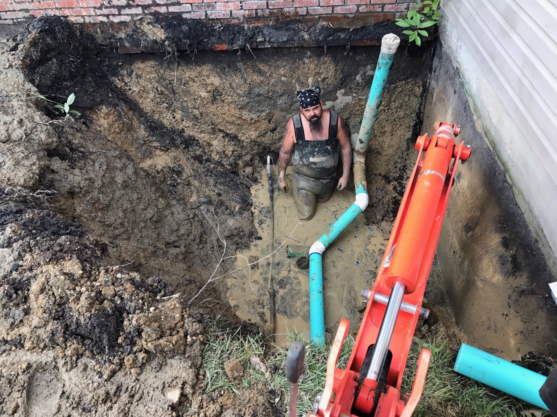 A man is kneeling in the dirt next to a red excavator.