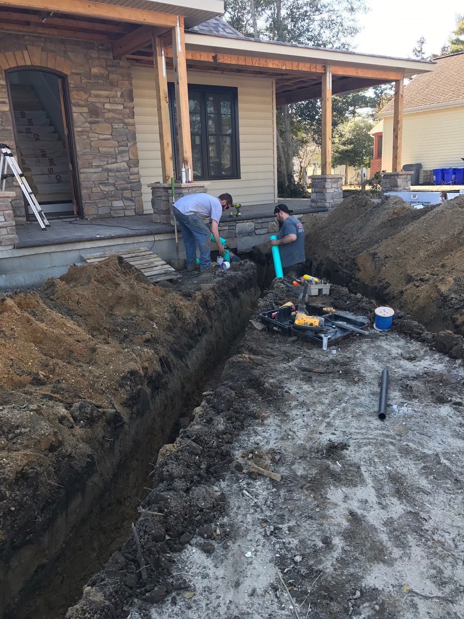 Two men are digging a trench in front of a house.