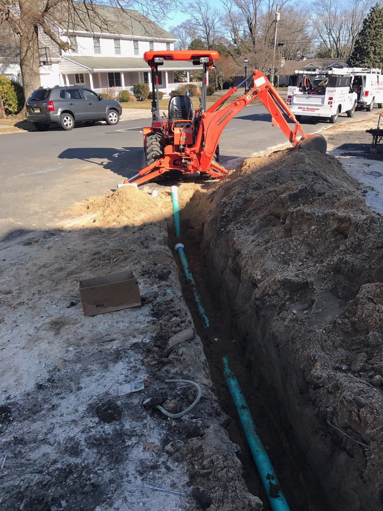 An orange excavator is digging a hole in the ground next to a green pipe.