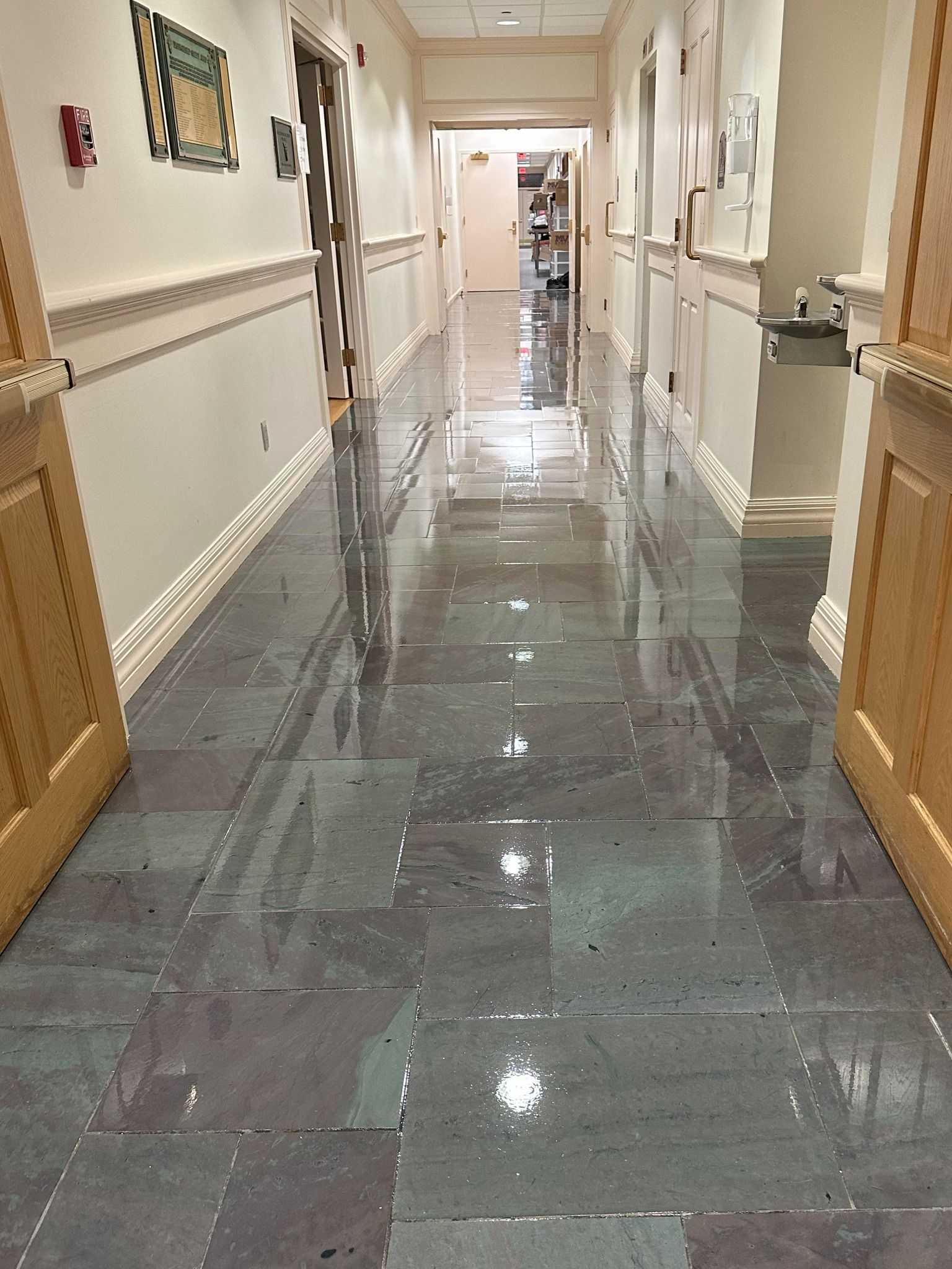 Hallway with wet, reflective tiled floor, doors on either side, and art on the wall.