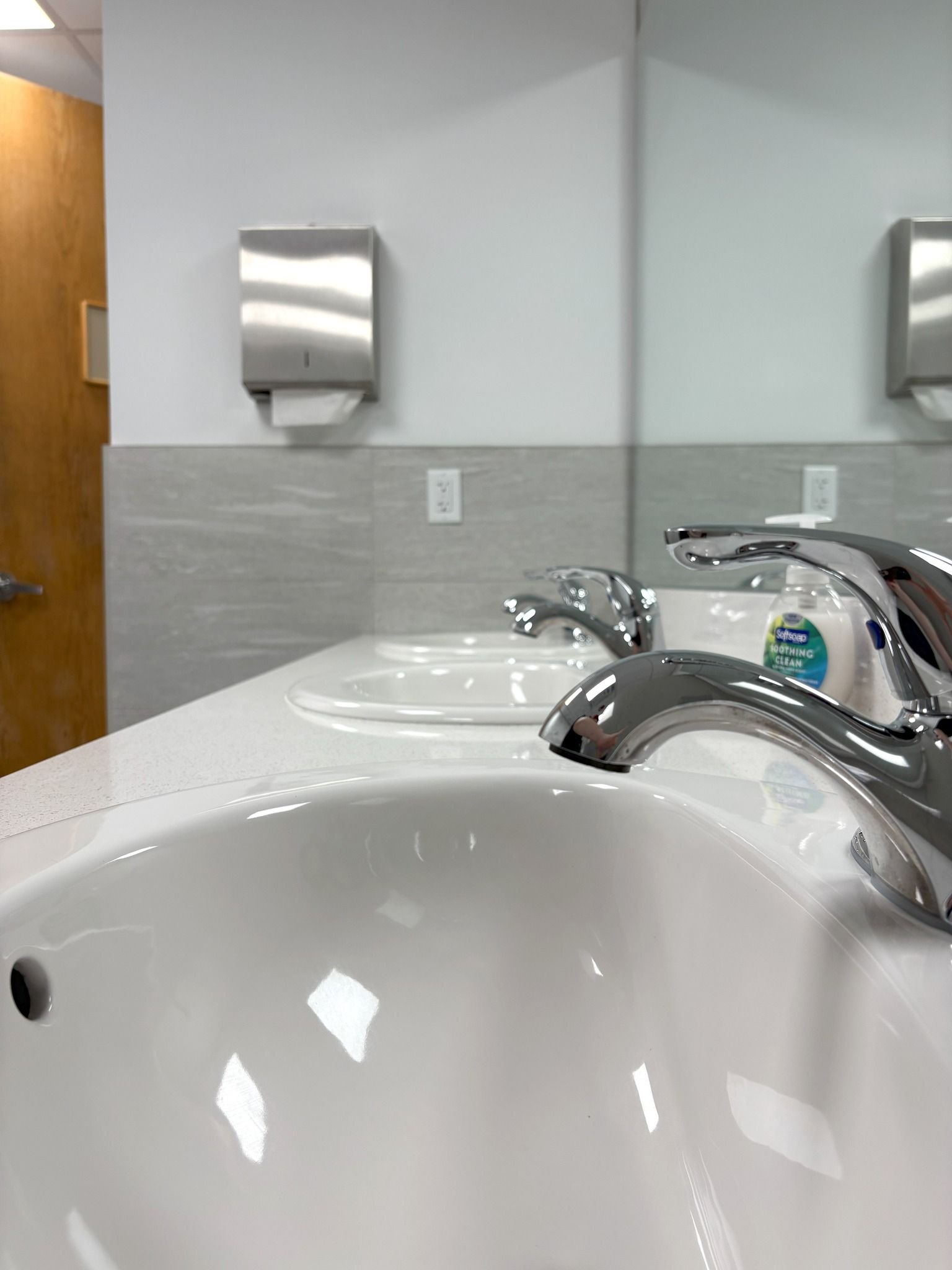 Bathroom with two white sinks, chrome faucets, and a paper towel dispenser mounted on the wall.