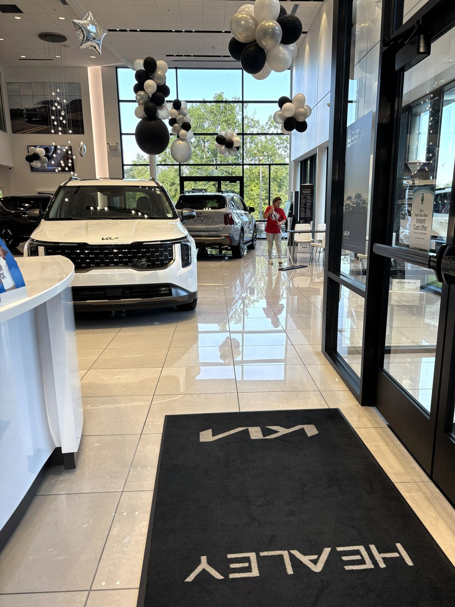 The interior of a car dealership featuring a white Kia SUV, black and white balloon clusters, and a branded floor mat.