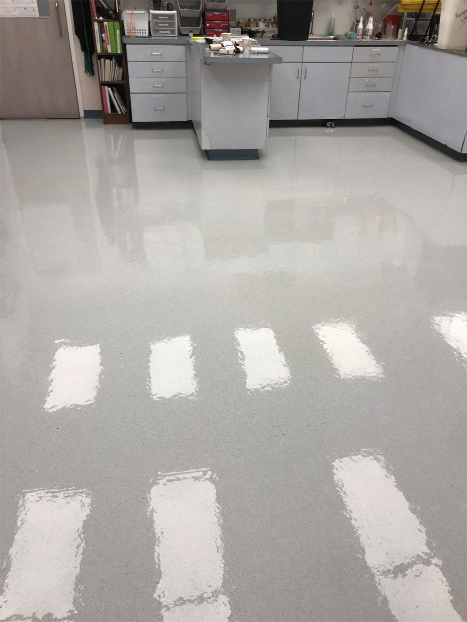 A high-angle view of a grey, polished laboratory floor reflecting rectangular ceiling lights.