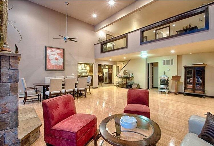 Spacious living room with high ceilings, fireplace, dining area, red armchairs, and loft overlooking.