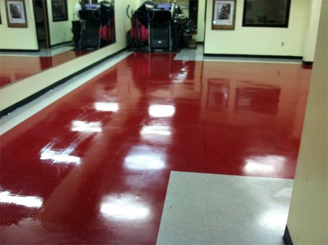 A glossy, bright red floor in a room with exercise equipment and framed pictures on the walls.