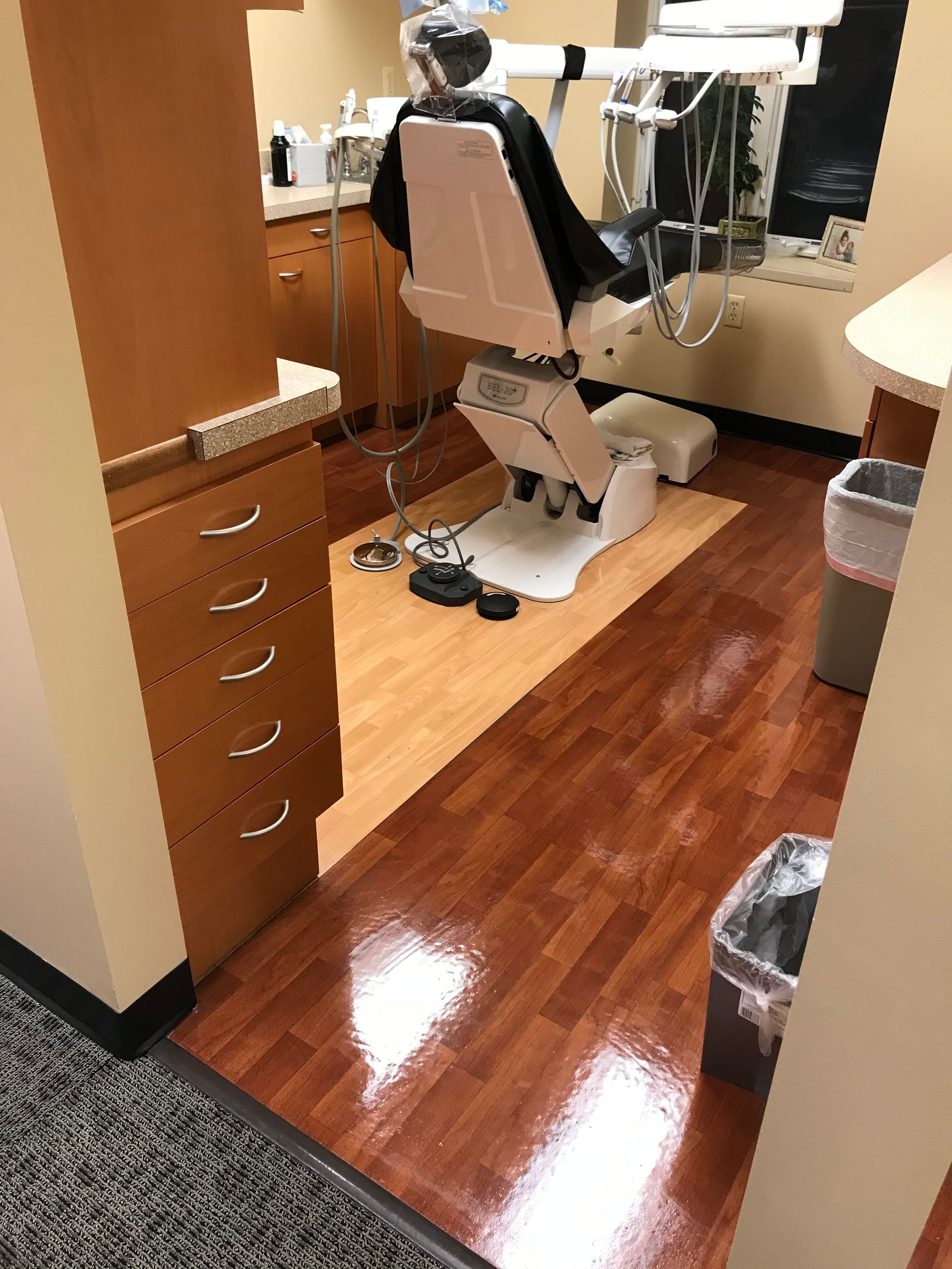 Dental office exam room with dental chair, cabinets, and wood-look flooring.