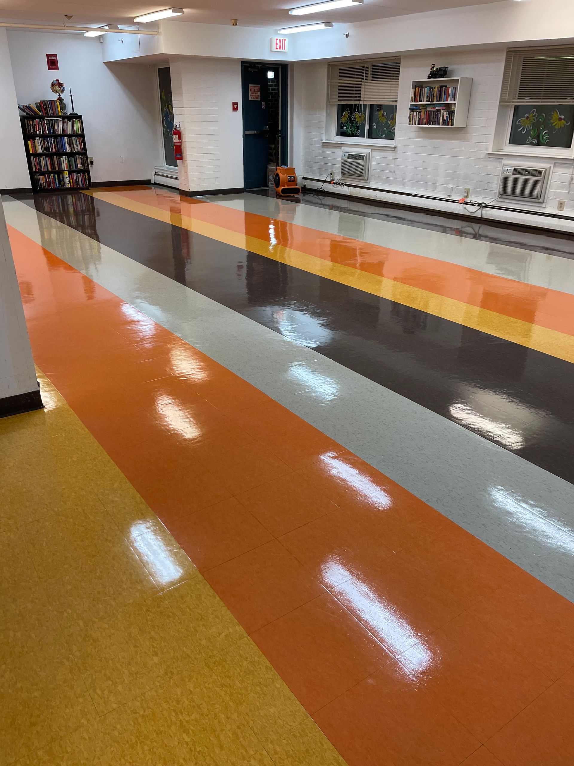 Colorful striped floor in a room. Orange, brown, gray, and yellow strips. White wall with vents.