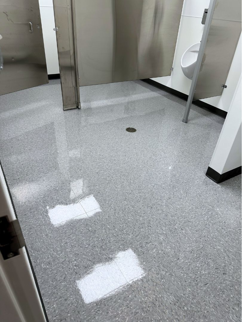 Public restroom with gray speckled floor, stalls, and a urinal.
