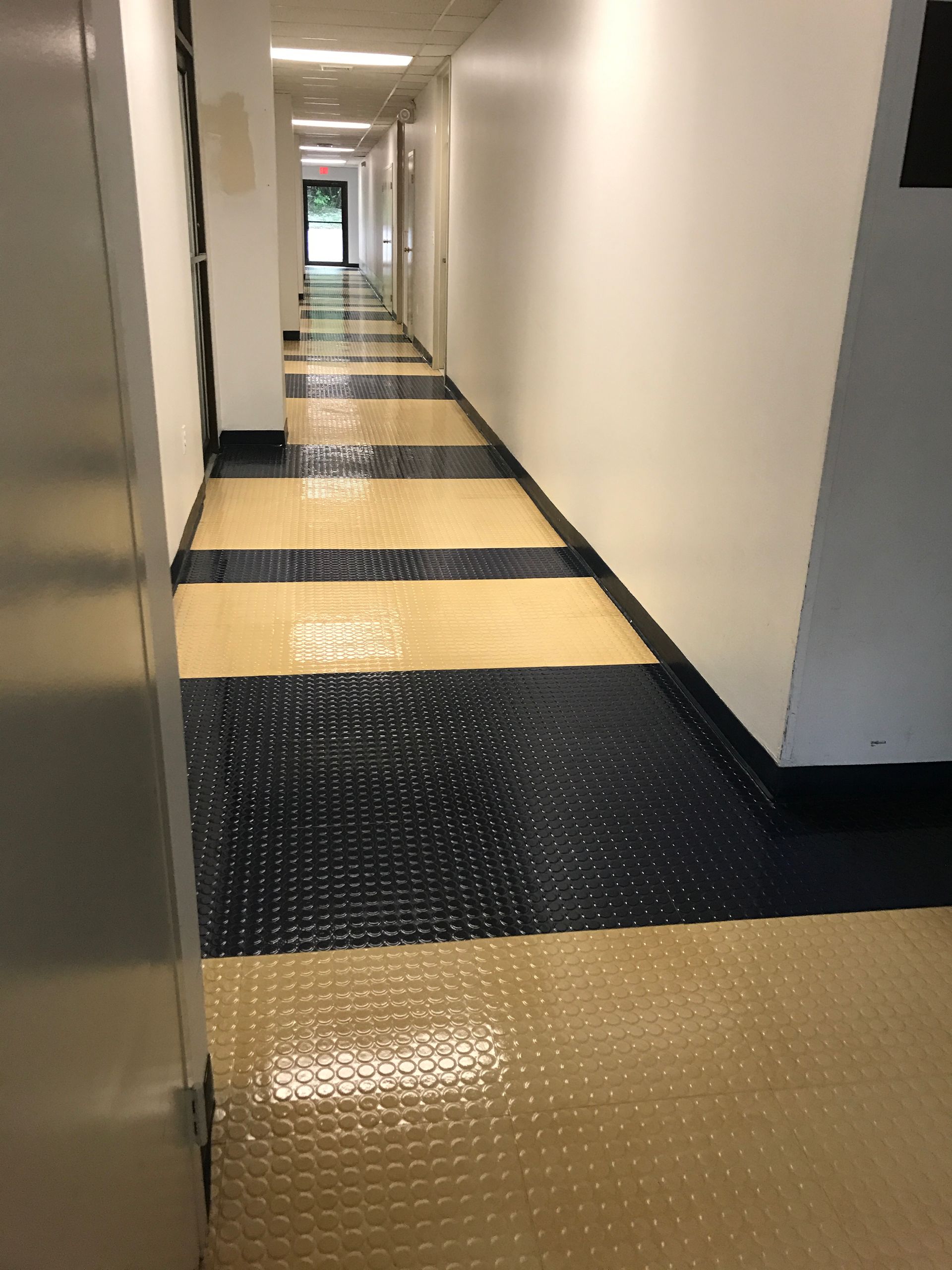 Hallway with alternating tan and navy patterned floor, white walls, and a door at the end.