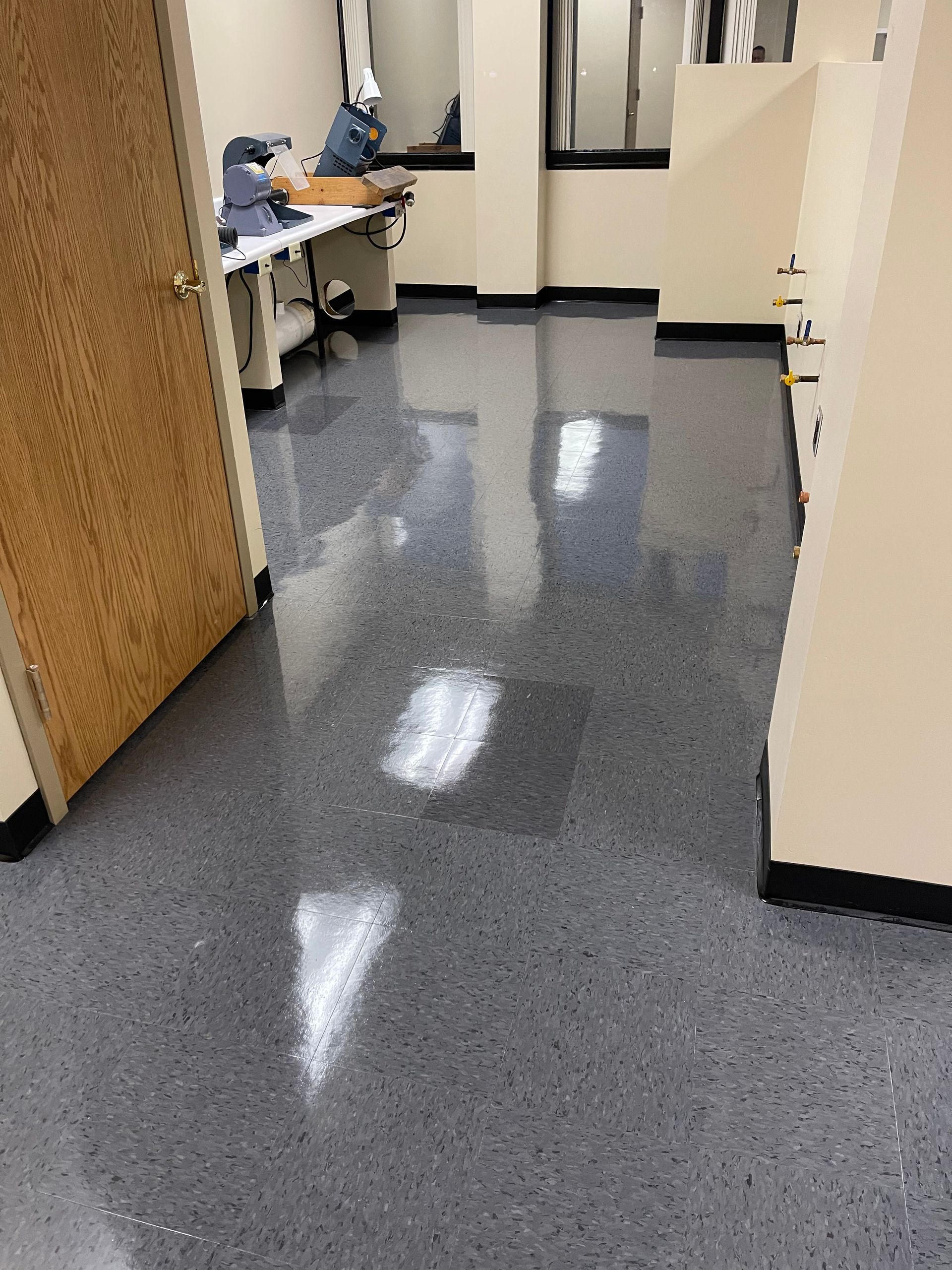 Gray speckled floor in an office. Ajar wooden door on the left, office cubicles and desk visible in the background.