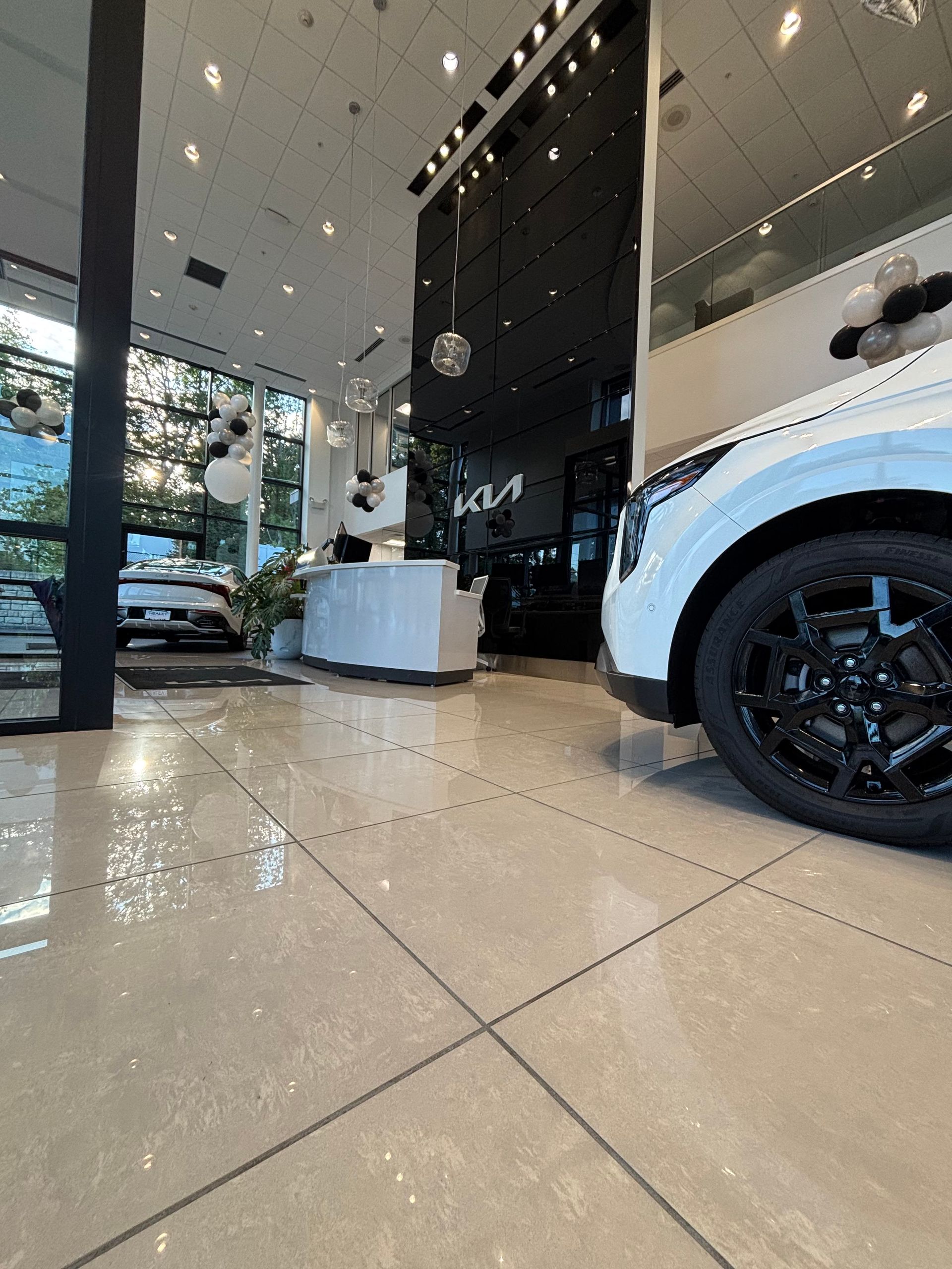Kia car showroom interior with white car, black wheels, and tiled floor.