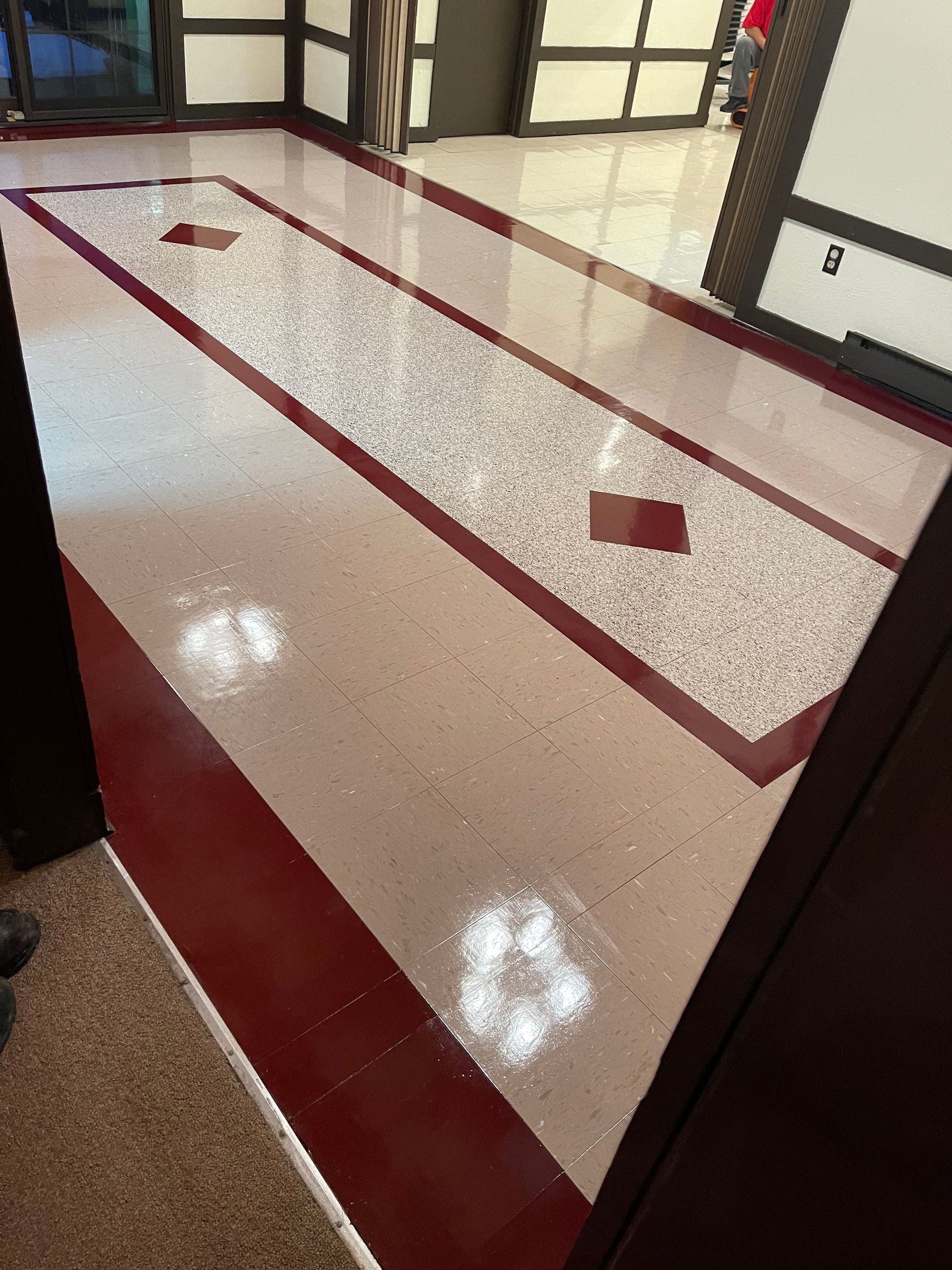 Shiny red and speckled floor with a maroon border and accents in a building hallway.
