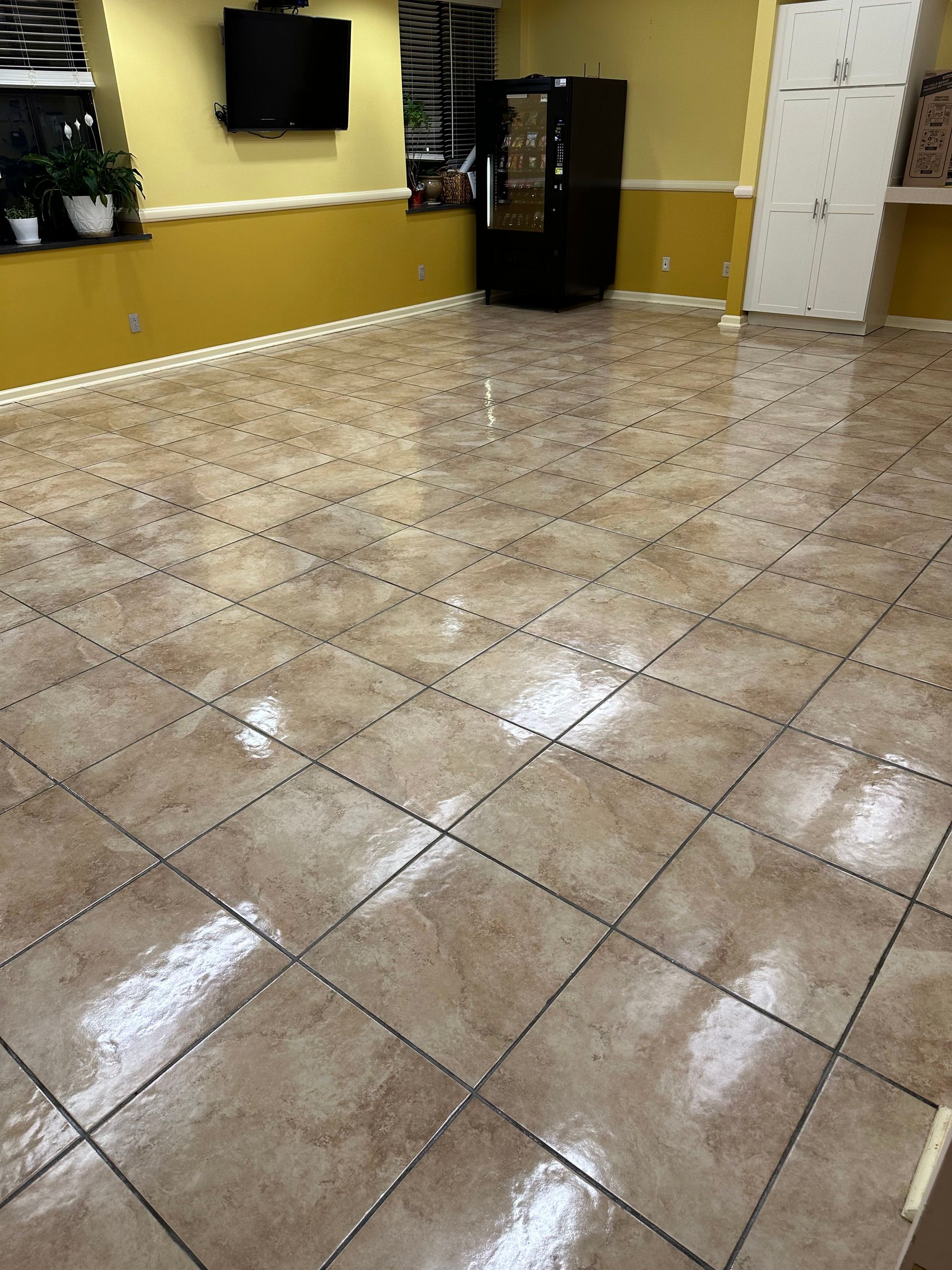 A tiled room with light brown patterned floors, a black vending machine, a mounted TV, and a white cabinet against walls.