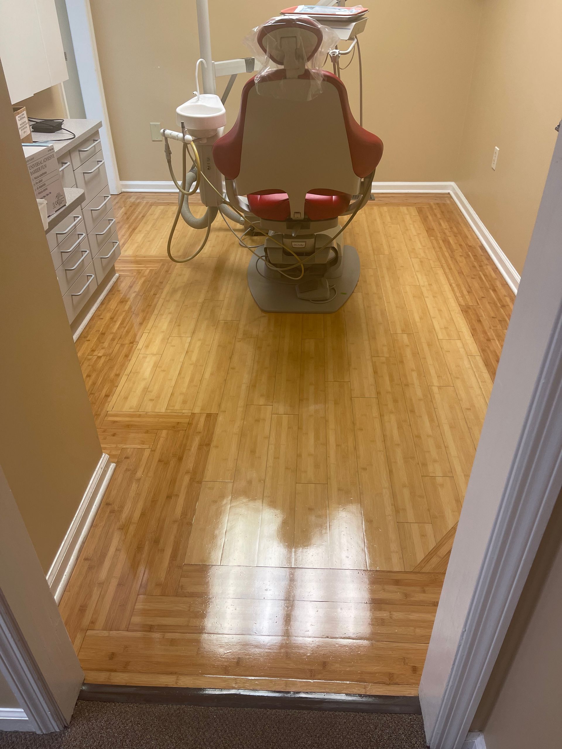 A dental exam room with a red chair, dental equipment, and light wood flooring, viewed from a doorway.