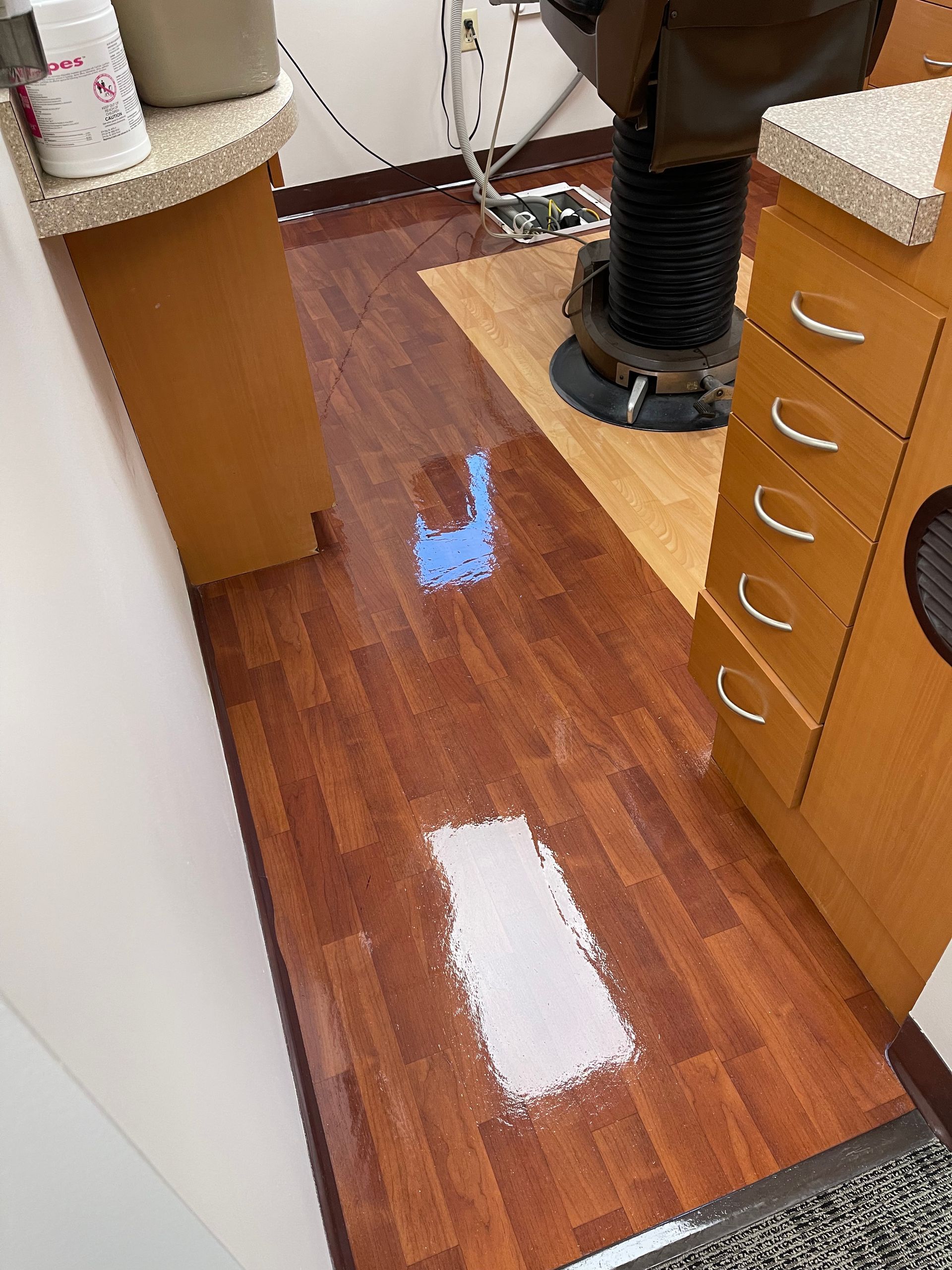 A salon floor featuring one blue and one white rectangle painted on the wood-look flooring between cabinets and a chair.