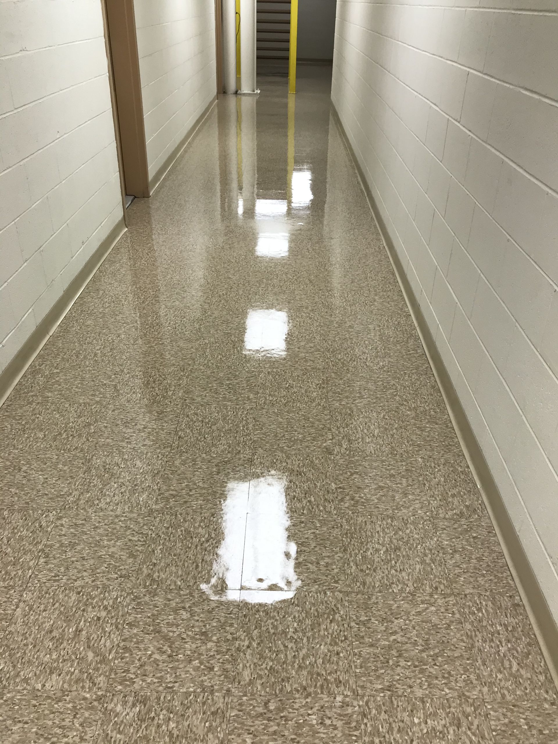 A long, narrow hallway with white concrete block walls and a glossy, speckled beige floor reflecting overhead lights.