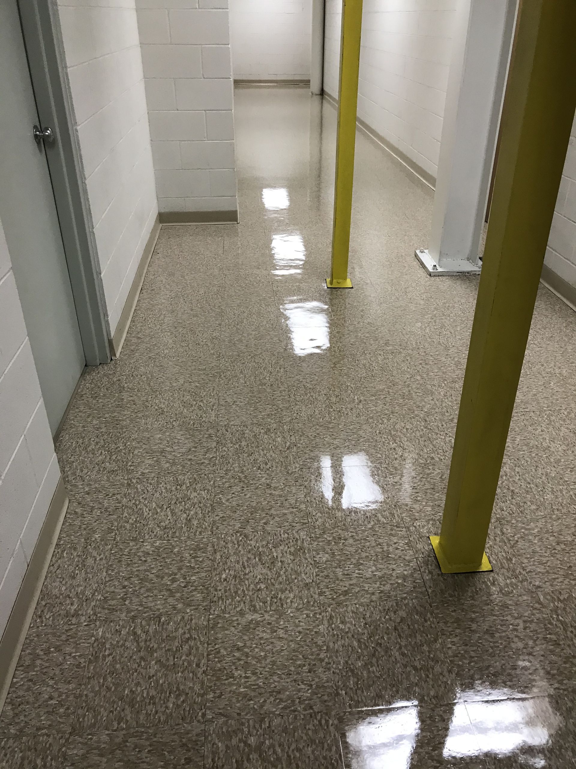 A hallway with a speckled, glossy epoxy floor, white cinder block walls, and two prominent yellow support pillars.
