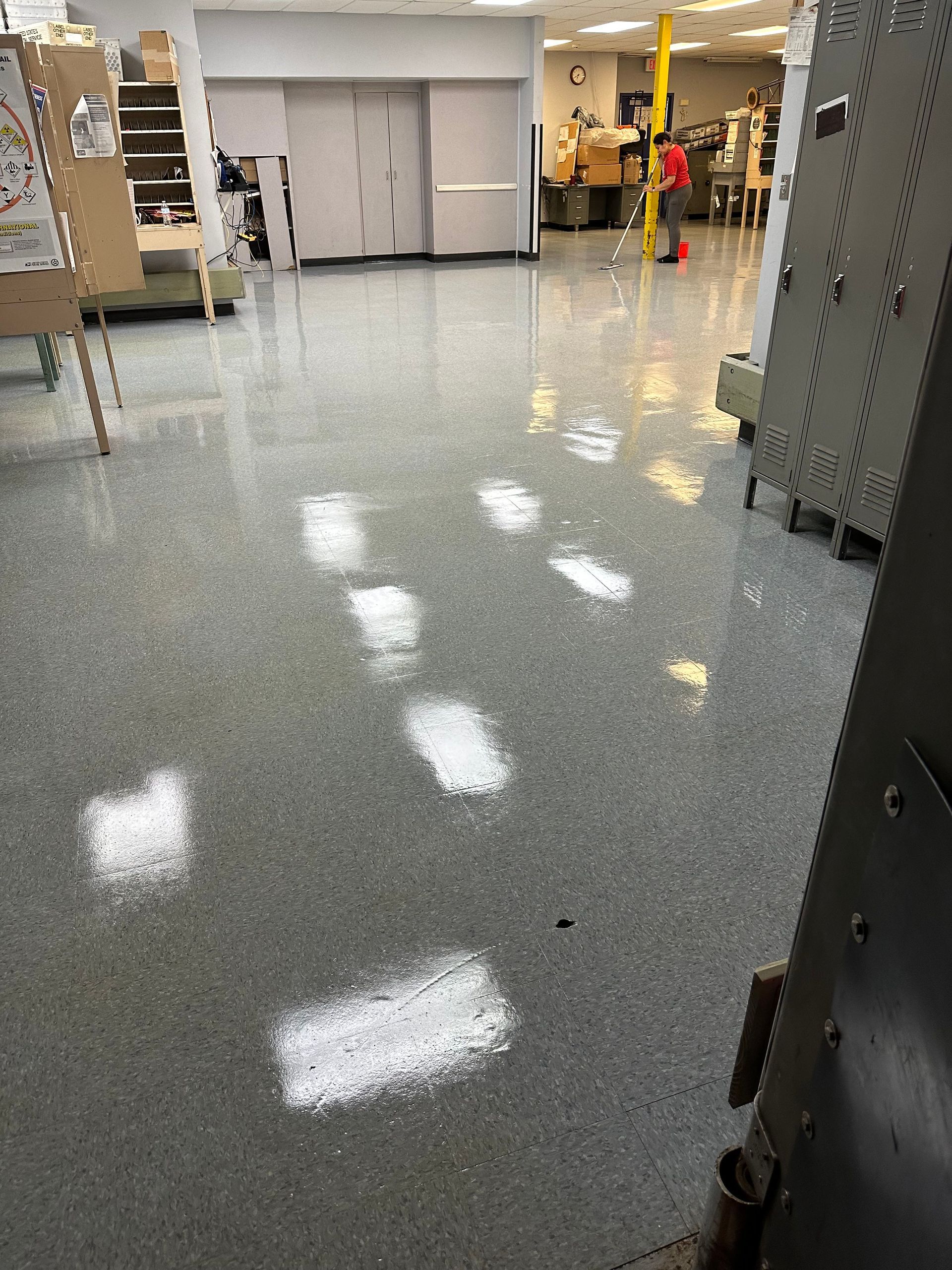 A shiny grey speckled epoxy floor in an industrial room with bright light reflections, with a person working in the back.